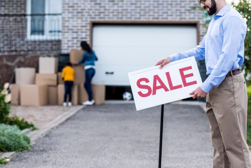 man placing sale sign in front of house